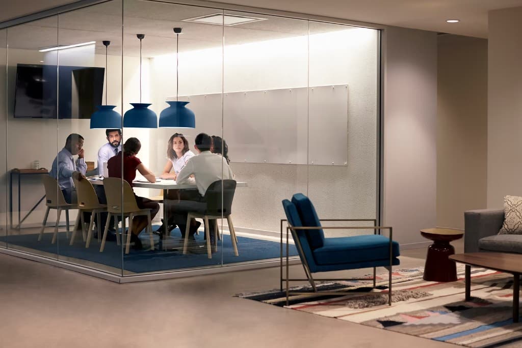 Professional team meeting in a bright modern office with glass walls, collaborating around a table.
